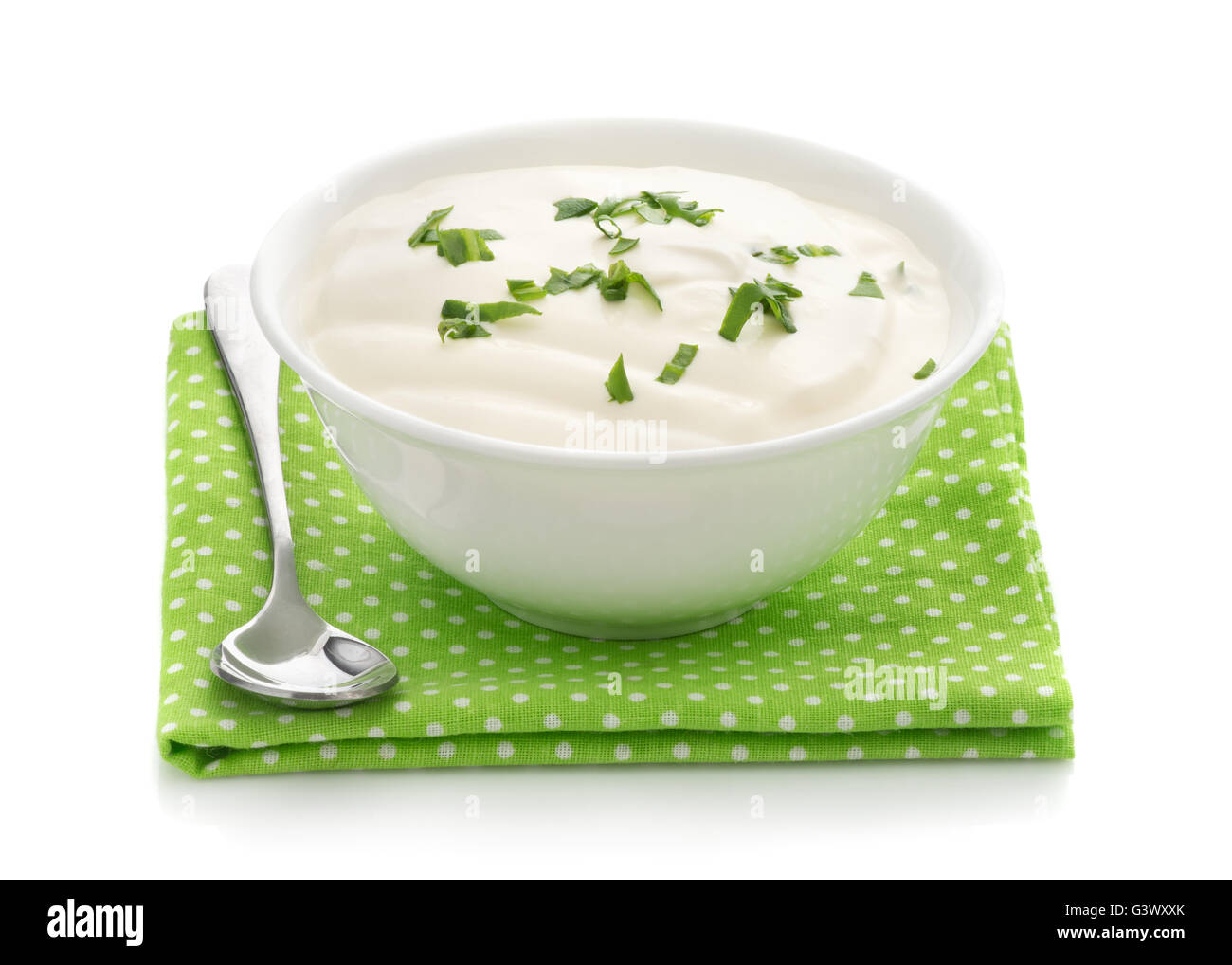Natural sour cream in a white bowl with chopped potherbs, spoon, green napkin isolated on a white background close up Stock Photo