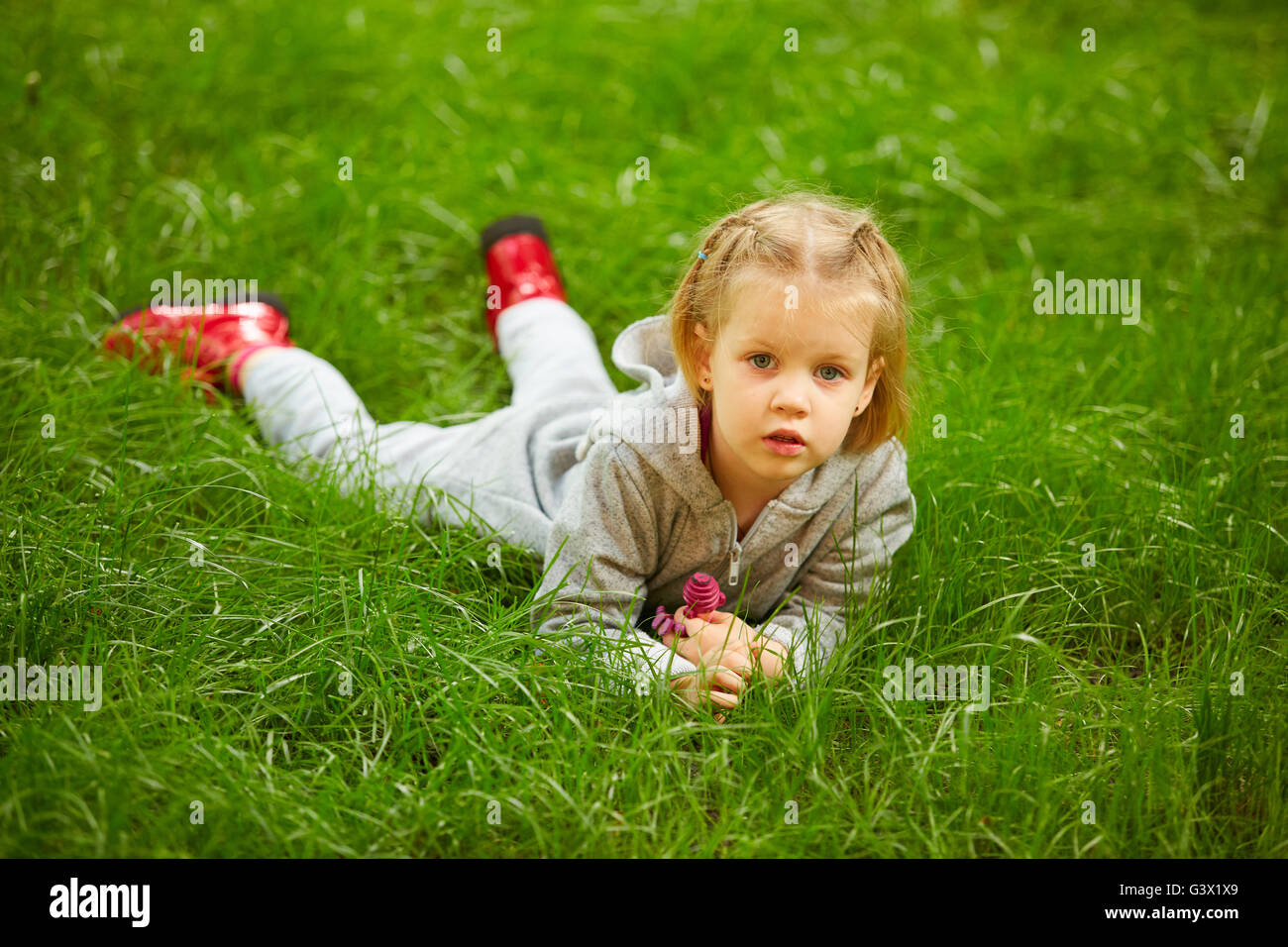 Portrait of a little girl lying on green grass Stock Photo - Alamy