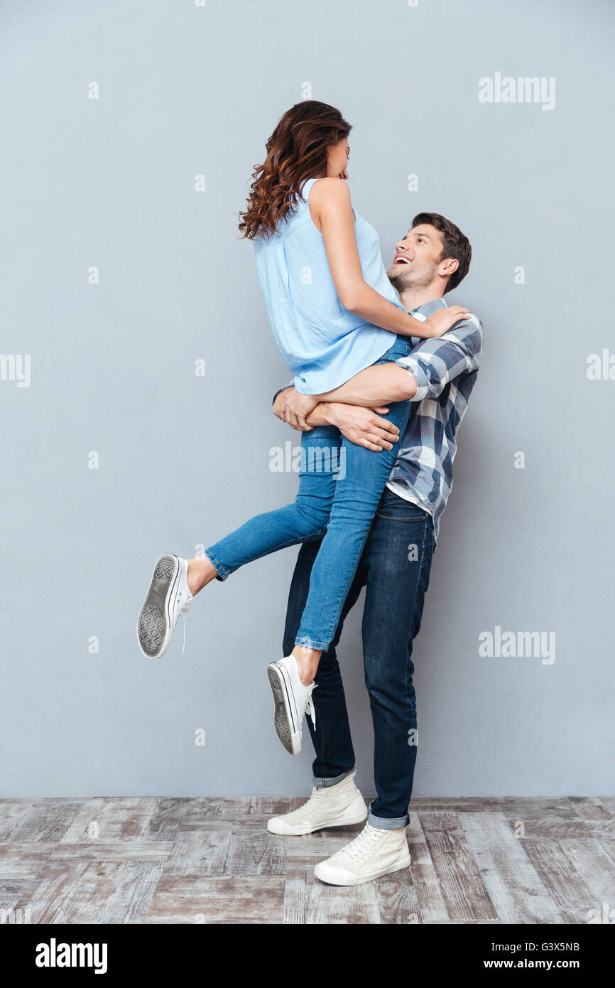 Man lifting up his girlfriend isolated on gray background Stock Photo