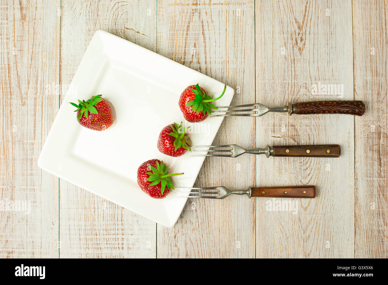 Three forks and ripe red strawberries on a white plate Stock Photo