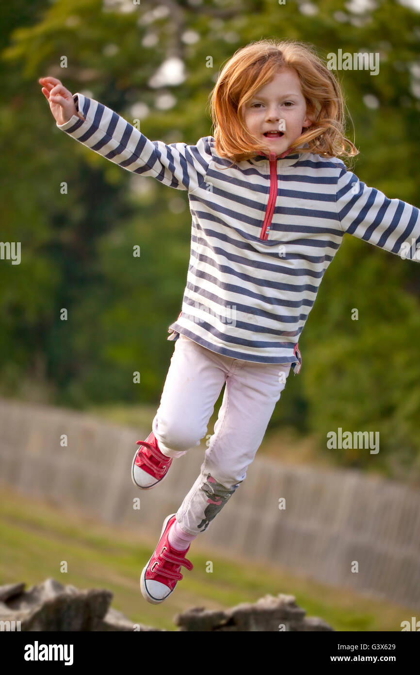 Jumping High. A  young girl attempts to spring off an old fallen tree trunk, to jump high in the air. Stock Photo