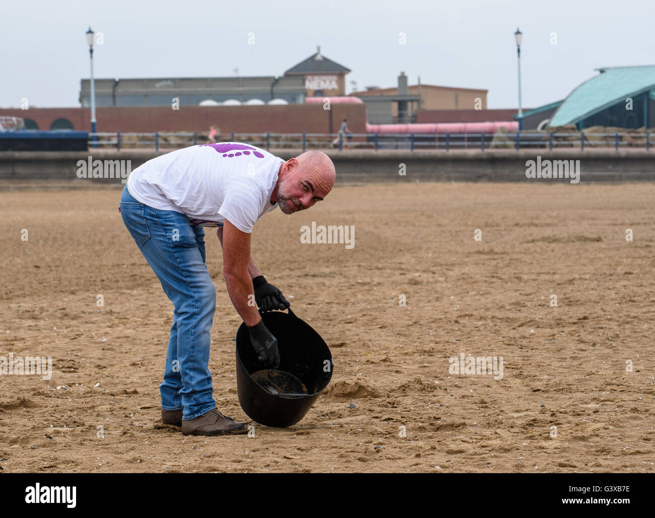 Man helping to clear litter and other rubbish from a sandy beach in Lytham St Anne's, Lancashire, UK Stock Photo