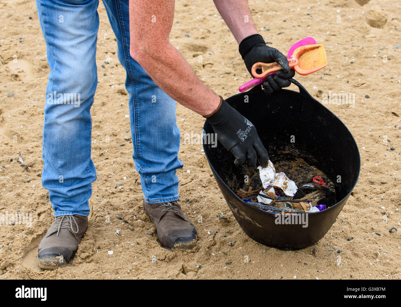 Image showing lower portion of man's body as he clears up litter from a sandy beach Stock Photo