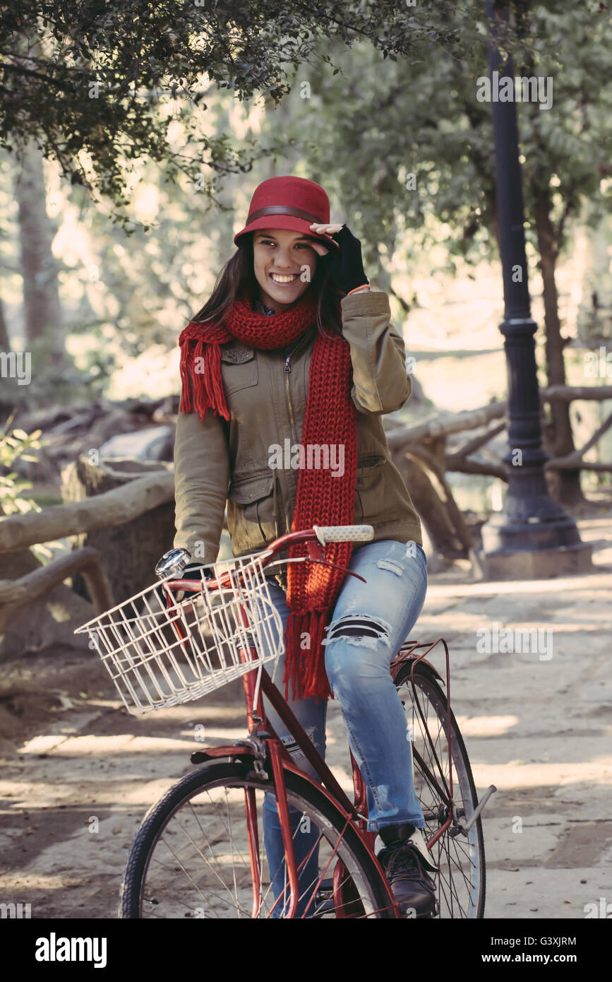 Happy vintage fashion girl riding bike in the park on a sunny autumn day, nature scenery background. Stock Photo