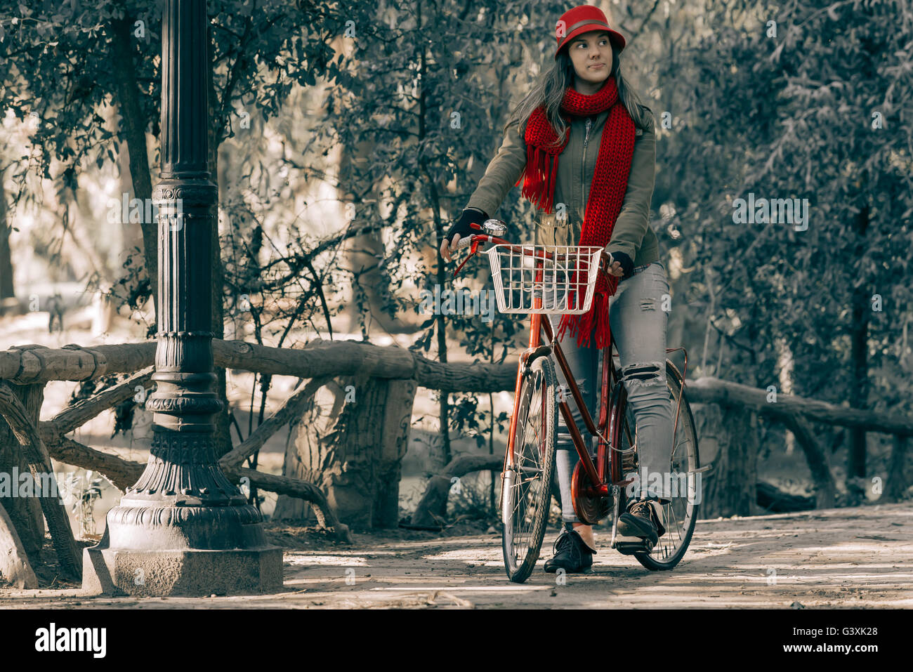 Girl riding bike at park wearing red urban fashion on beautiful autumn day, vintage contrast effect. Stock Photo