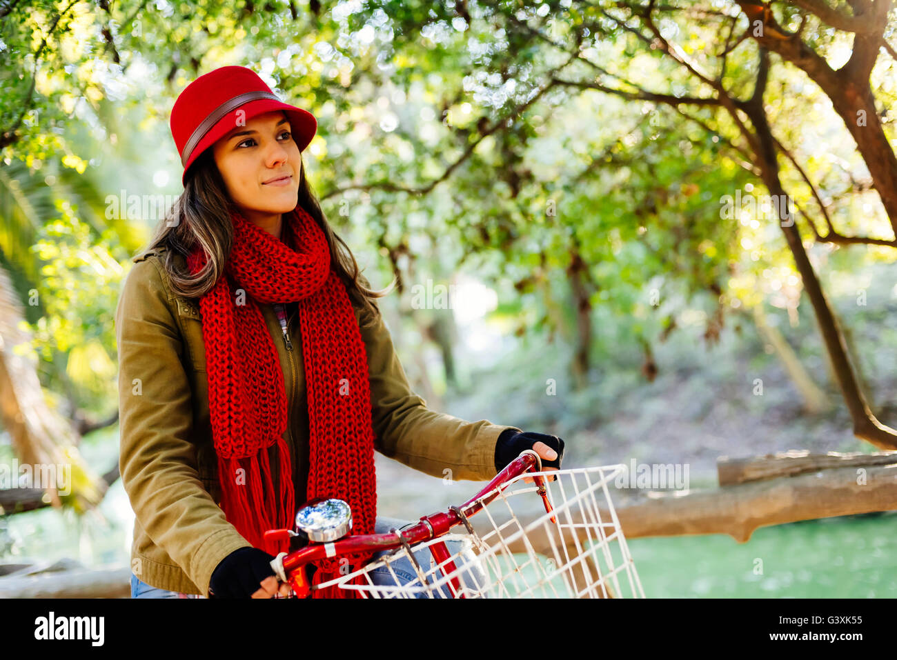 Trendy young woman smiling while riding vintage style bicycle on fall season, colorful nature scenery background. Stock Photo