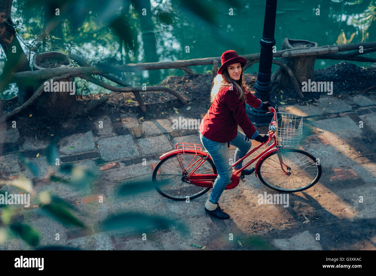Top angle view of happy woman riding bike on park in vintage urban fashion looking at camera, nature scenery background. Stock Photo