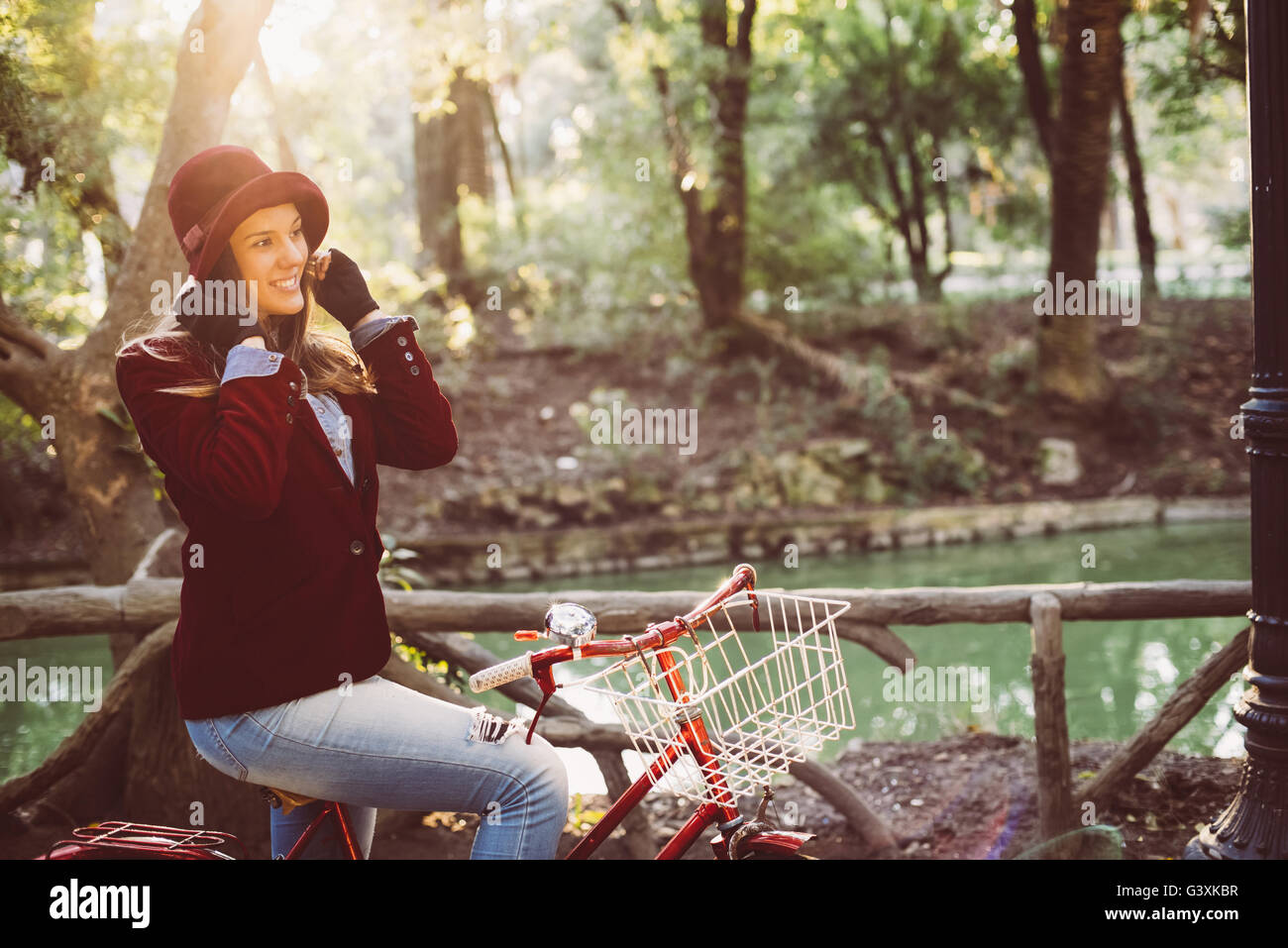 Happy young woman smiling while riding bike at the park on sunny autumn day, urban fashion style girl enjoying nature scenery. Stock Photo