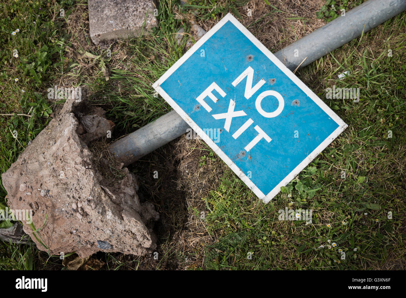 A knocked over 'No exit' sign lying on an uprooted sign pole. Stock Photo