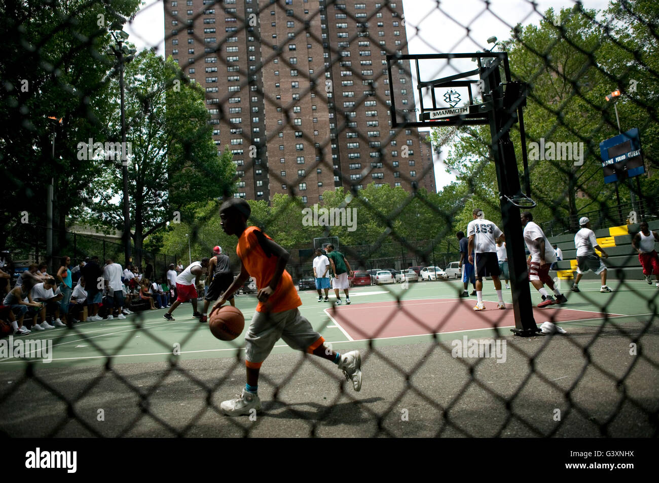 A boy passes behind the court where tryouts for the Rucker's street basketball tournament are taking place at Rucker Park in Har Stock Photo