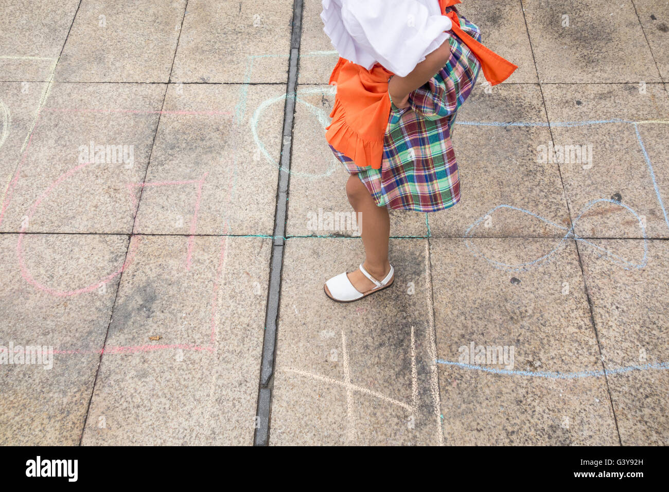 Young Spanish girl in traditional costume playing hopscotch at local fiesta in Spain. Stock Photo