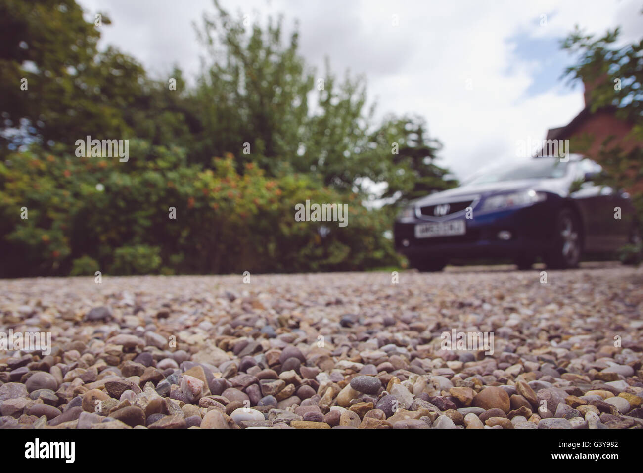 Car parked in front of the house. Focus on a little pebbles close to the camera. Stock Photo