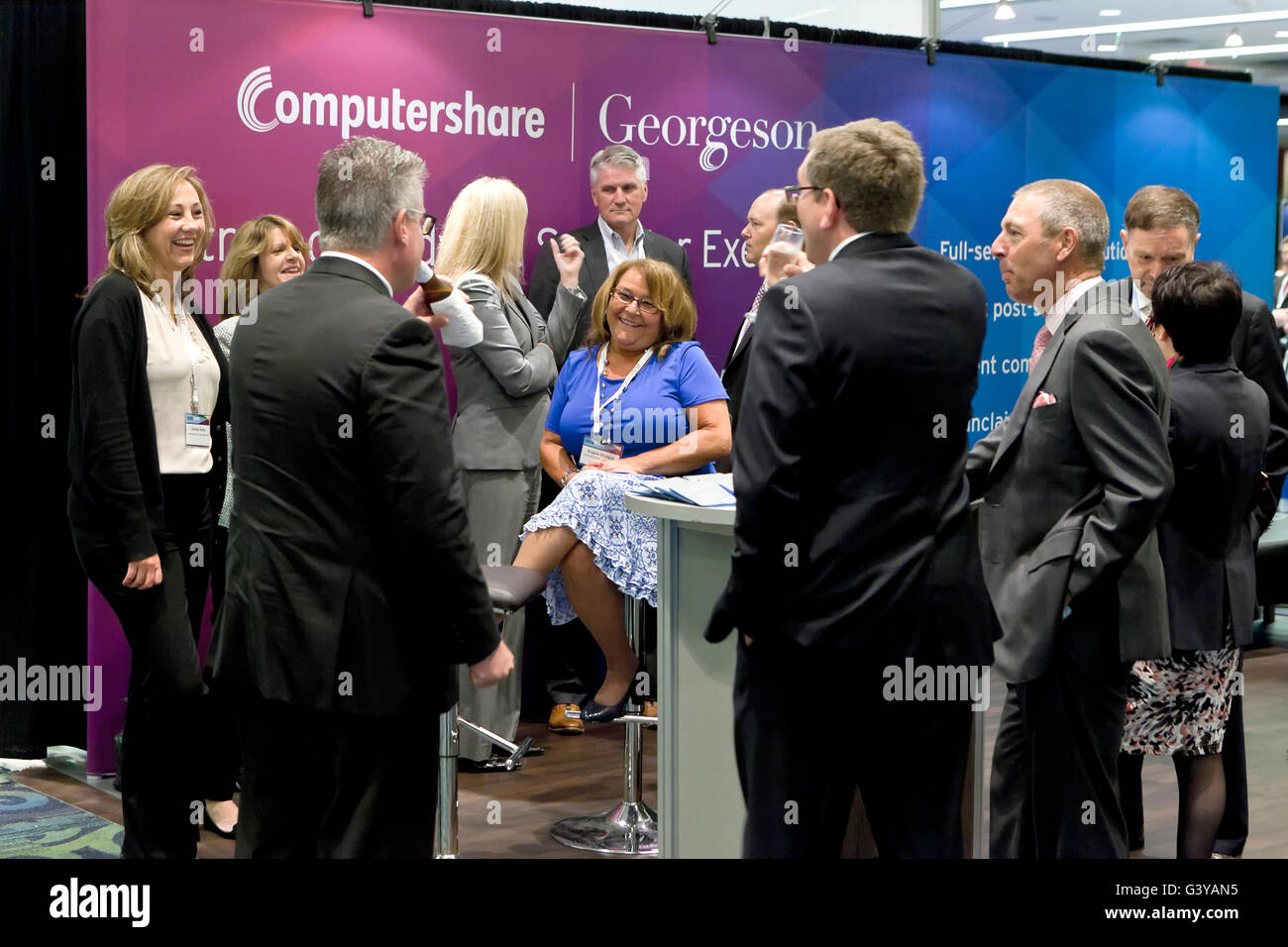 Businessmen and businesswomen discussing business and chatting in front of Computershare Georgeson booth at a business expo - USA Stock Photo