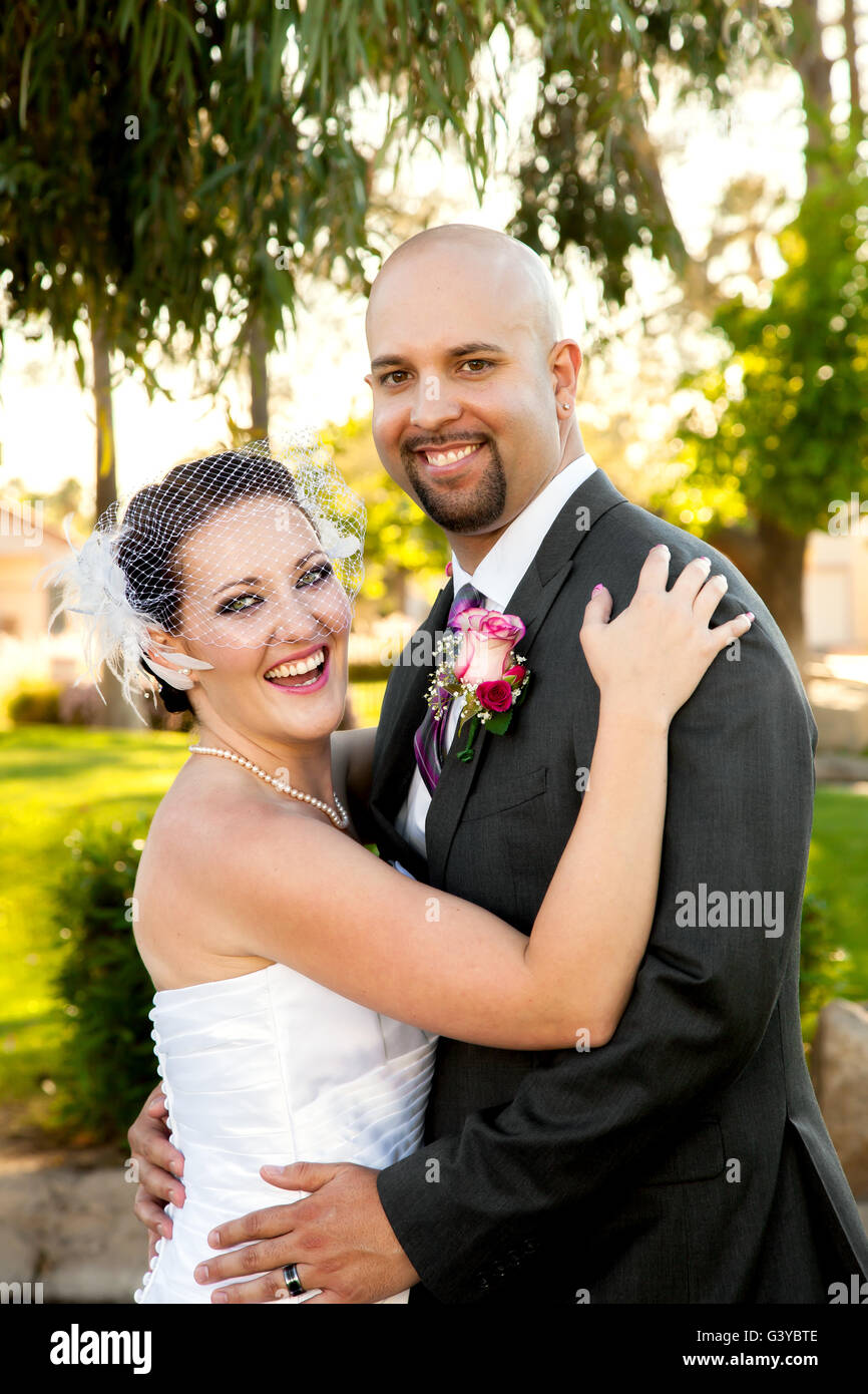 A bride and groom hold each other and laugh while looking at the camera.  They are happy and posed but unposed at the same time. Stock Photo
