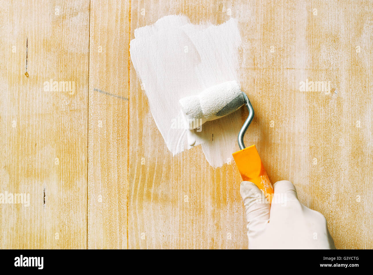 Hand with paint roller applying acrylic lacquer on wooden board, non toxic water based lacquer wood coating Stock Photo