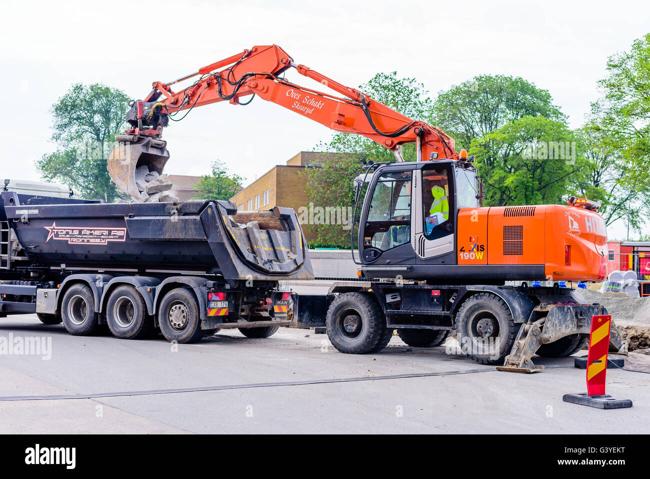 Karlskrona, Sweden - June 16, 2016: Orange Hitachi Zaxis 190W excavator digging out stones from a hole in a parking lot at Potth Stock Photo