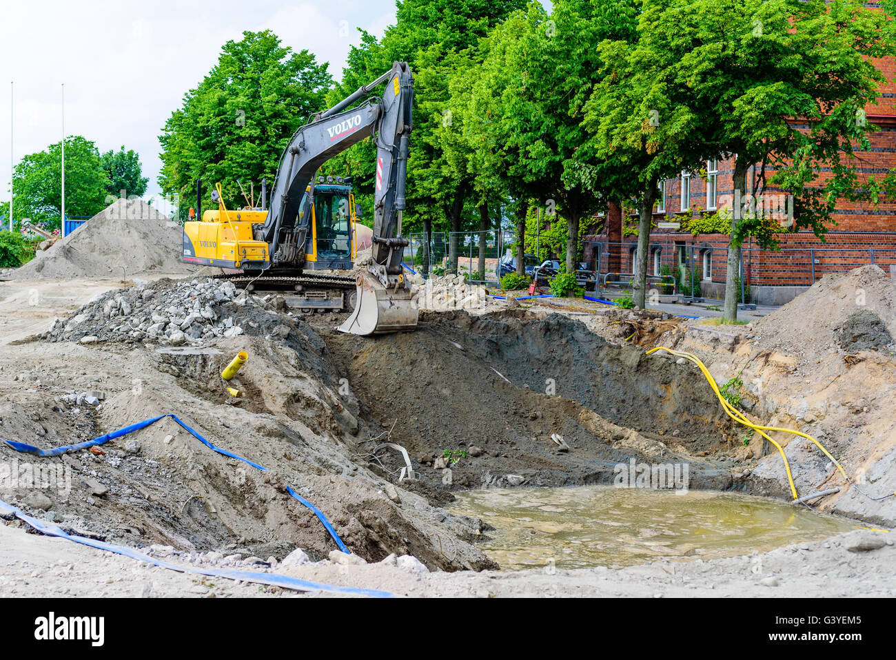 Karlskrona, Sweden - June 16, 2016: Yellow Volvo EC210 excavator digging a large hole in the ground. Water is filling up in the Stock Photo