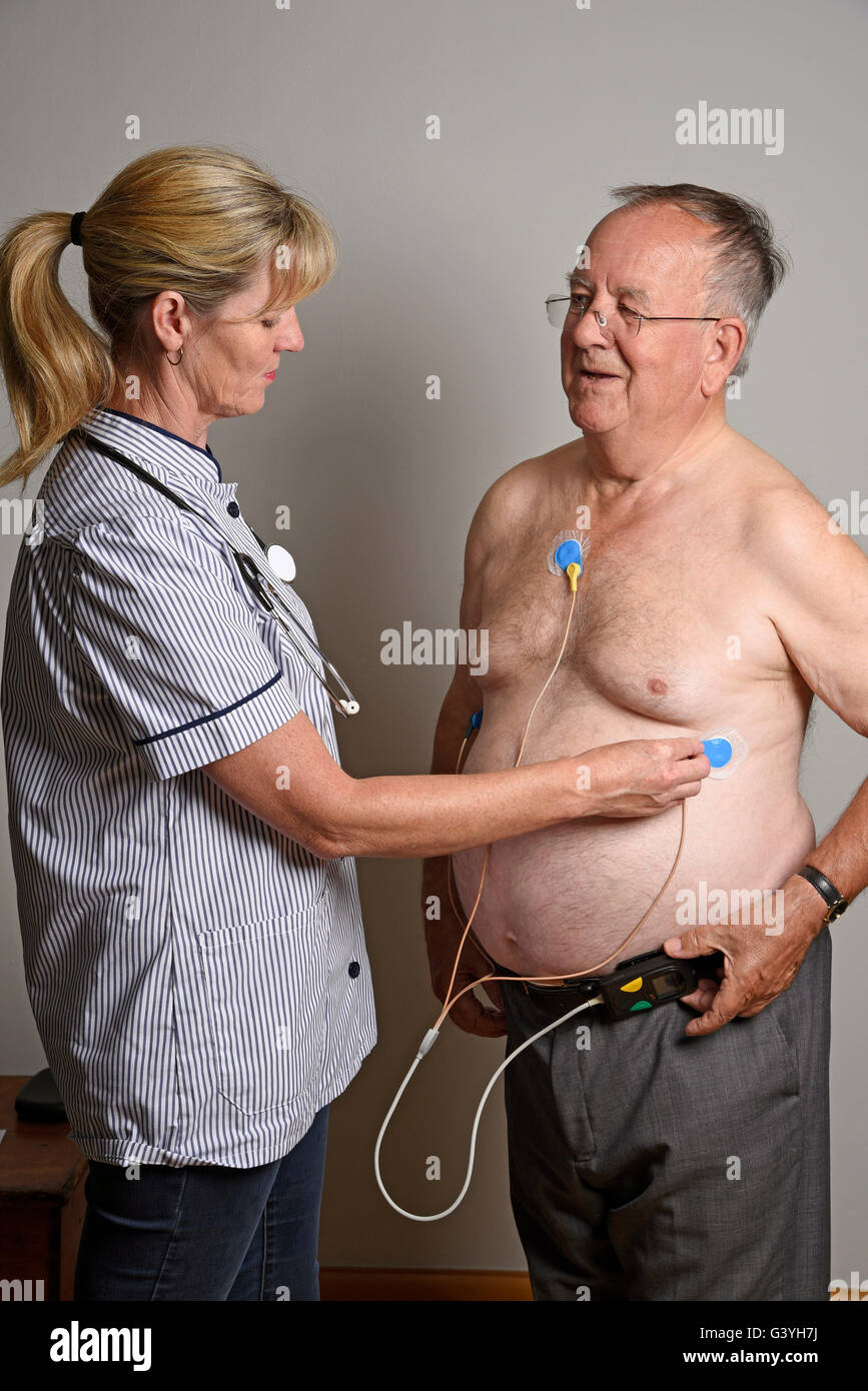 Member of a hospital cardiac measurement team installing a ambulatory ECG monitor to an overweight male patient Stock Photo