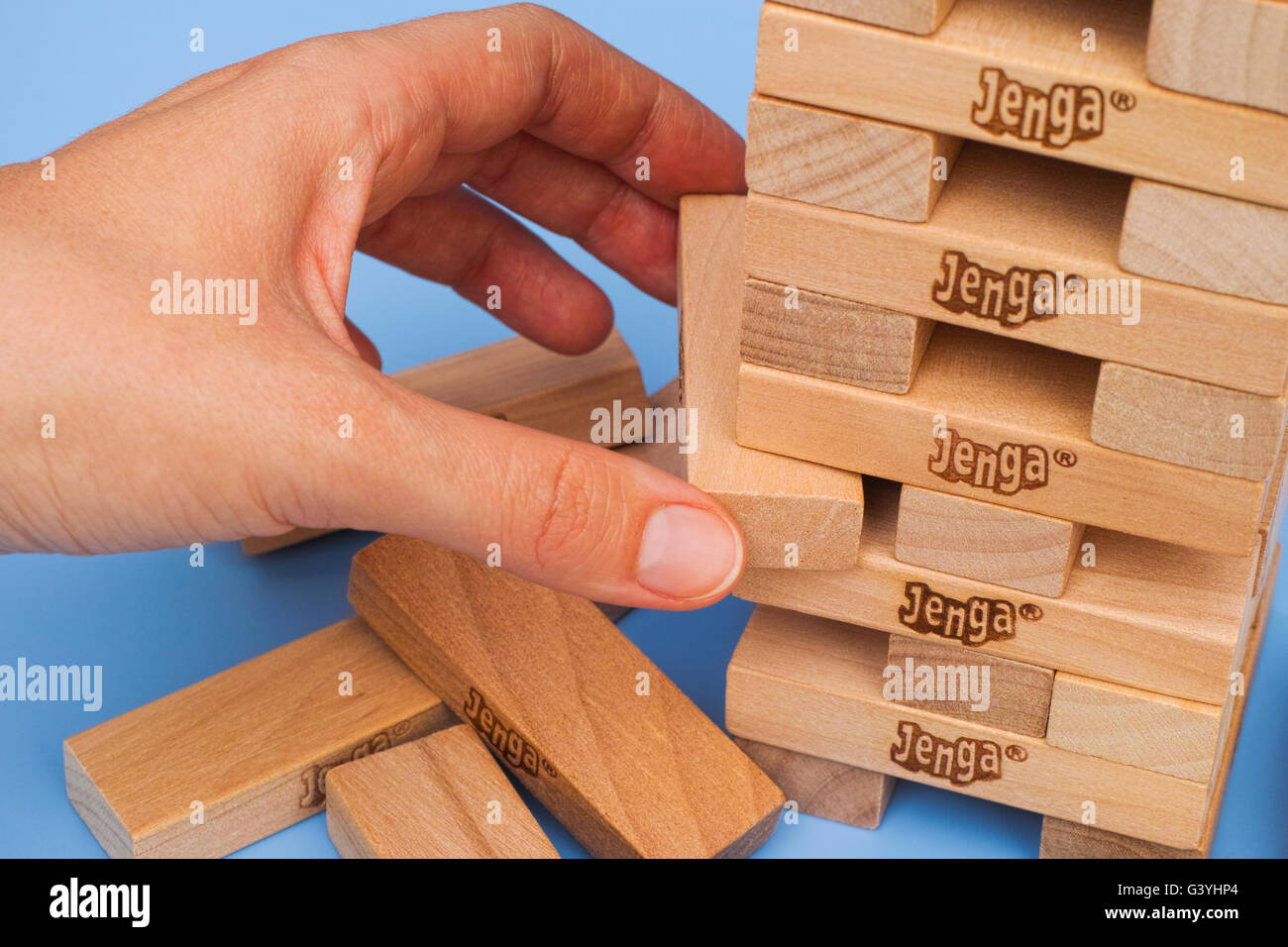 Tambov, Russian Federation - March 03, 2016 Human hand removing one block from Jenga tower constructed on blue background. Stock Photo