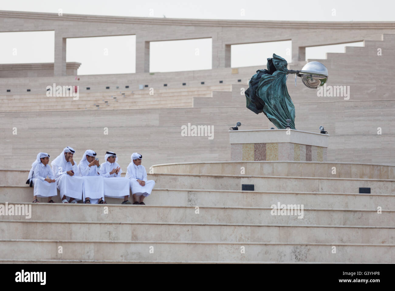Qatari boys in traditional dress sitting in the amphitheatre at Katara Cultural Village next to Force of Nature statue. Qatar Stock Photo