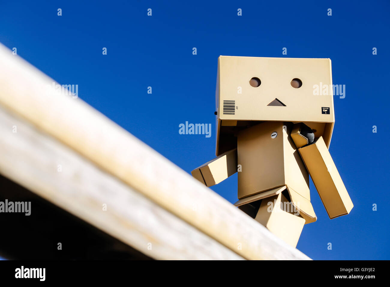 A Danbo Danboard fictional Robot Character walking along a wooden rail against a deep blue sky Stock Photo