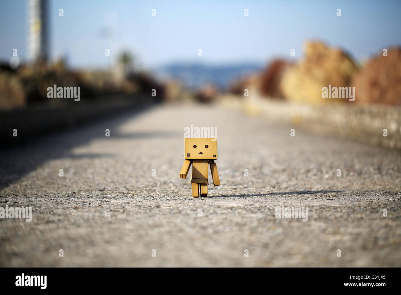 A Danbo Danboard Robot Character walking along a concrete path. is a fictional cardboard box robot character from Kiyohiko Azuma's manga series Stock Photo