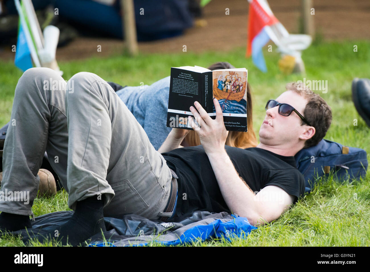 A man lying on his back reading a book  visiting attending enjoying themselves in the warm sunshine  at  the Hay Festival of literature and the arts , Hay on Wye, Powys, Wales UK, May 2016 Stock Photo