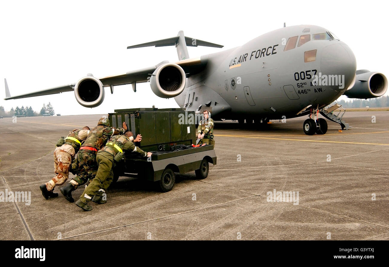 Airmen push a diesel generator in place after the C-17 Globemaster III lands. Stock Photo