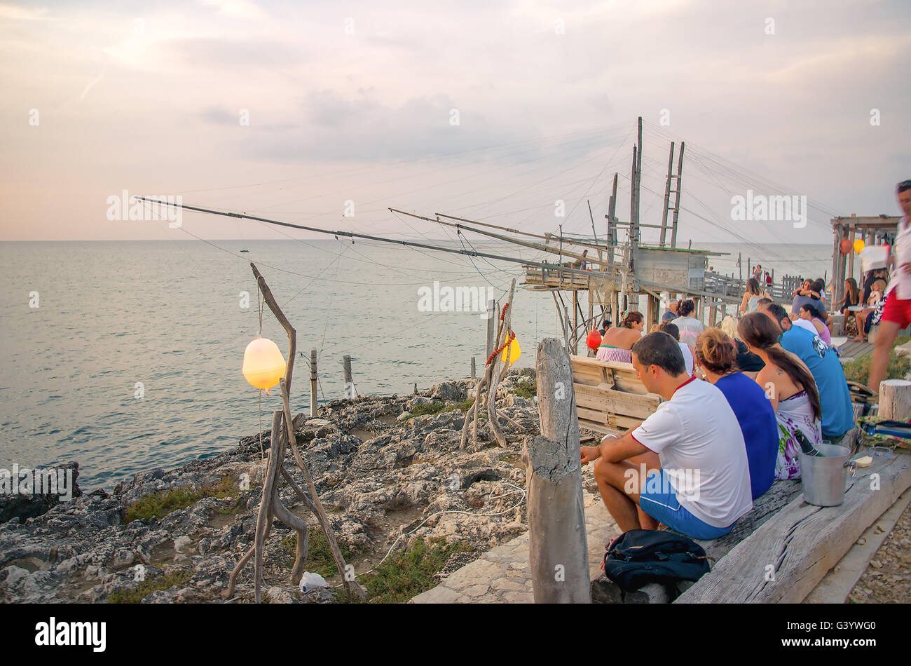 Peschici people get aperitif drink on the sea during sunset traditional fishing machine called Trabucco Stock Photo
