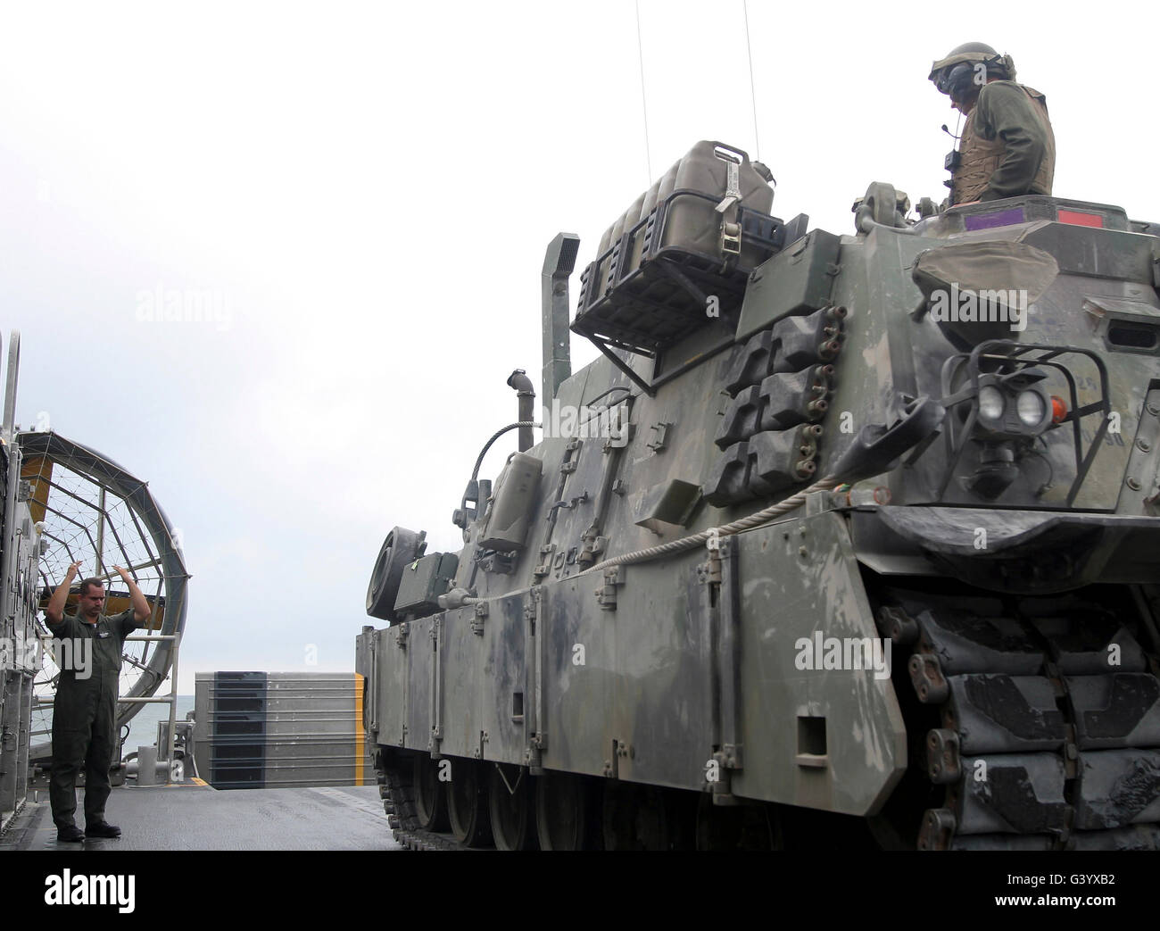 A Landing Craft, Air-Cushioned loadmaster signals the crew of an M88A2 Hercules Recovery Vehicle. Stock Photo
