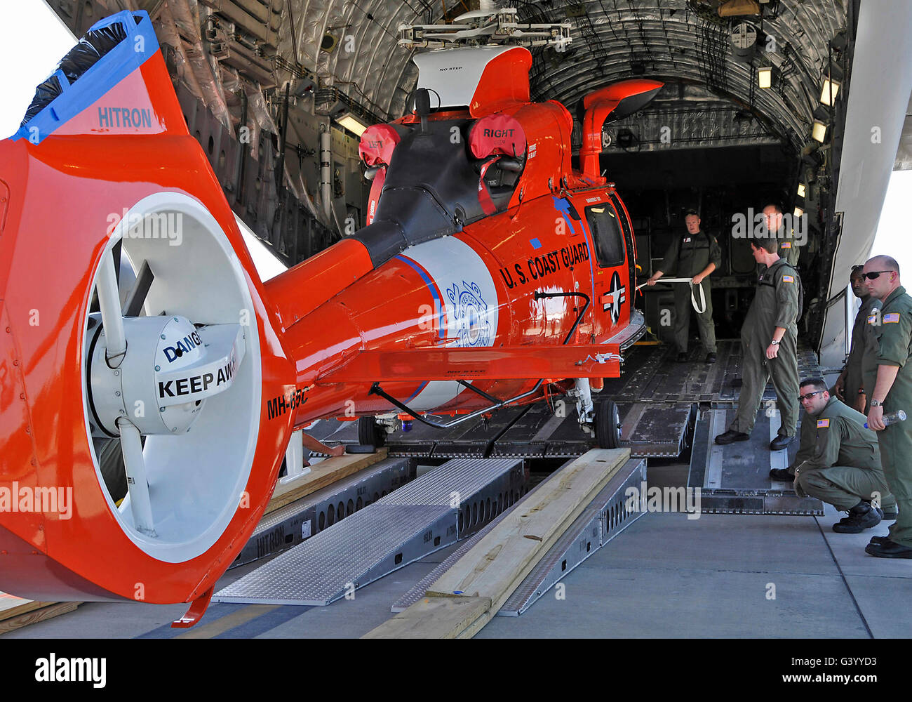 An aircrew loads a Coast Guard HH-65 Dolphin helicopter onto a C-17 Globemaster III. Stock Photo