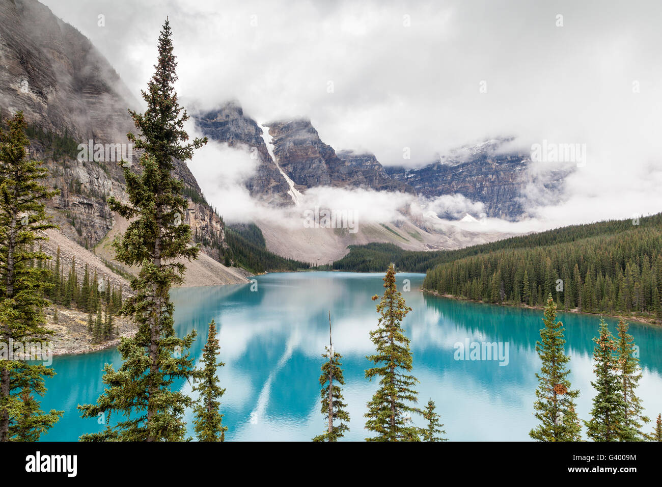 Fog and clouds descend onto the Valley of the Ten Peaks where glacier-fed Moraine Lake gives off its distinct turquoise blue col Stock Photo