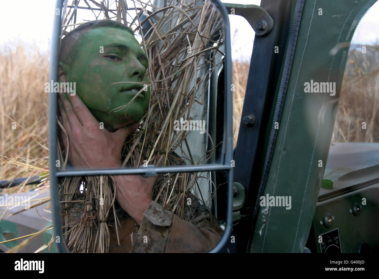 A scout observer applies camouflage paint after donning his homemade ghillie suit. Stock Photo
