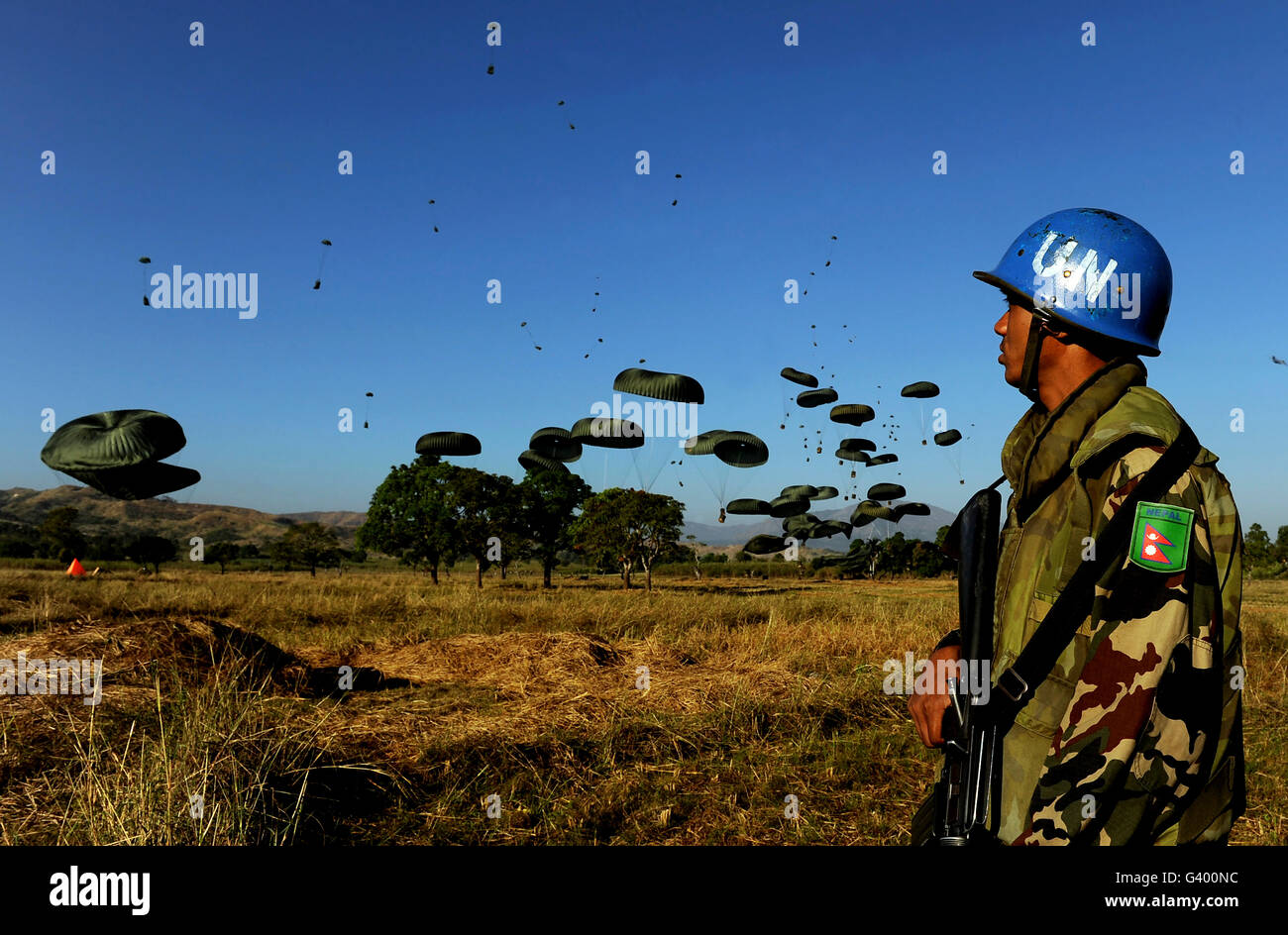A Nepalese service member watches as pallets of humanitarian aid fall to the ground. Stock Photo