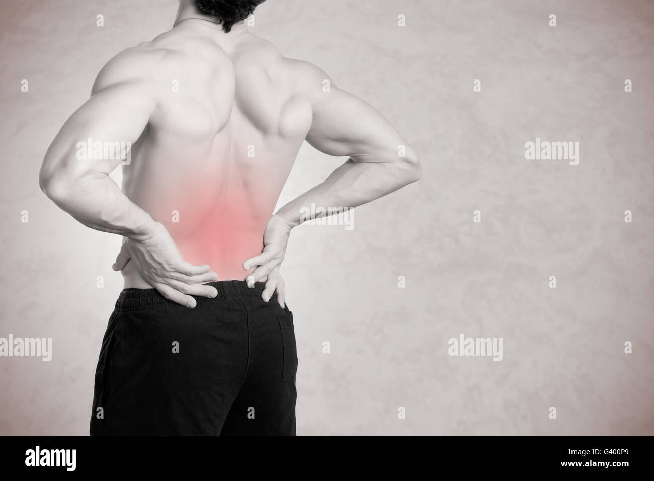 Male athlete with pain in his lower back, isolated in grey Stock Photo