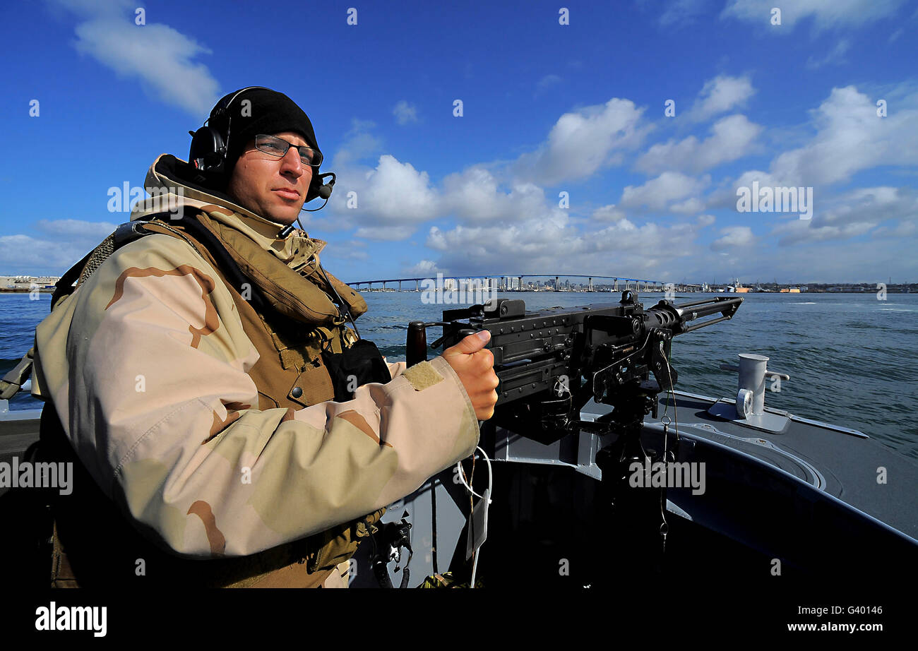 Gunner's Mate mans an M2 HB .50-caliber machine gun on the forward mount of a rigid-hull inflatable boat. Stock Photo