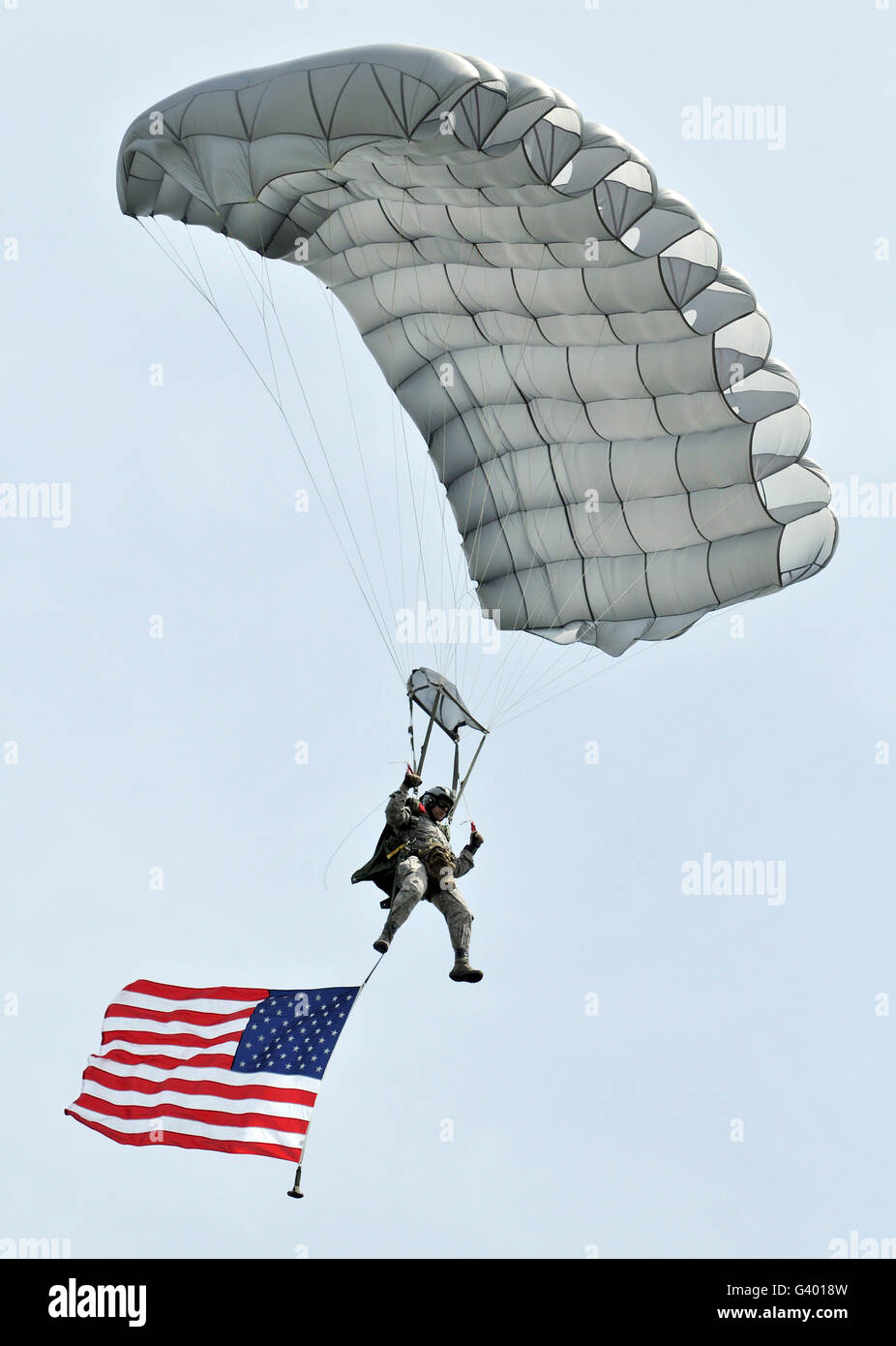 A parachutist flies the American flag over the Iron Mike drop zone in Normandy, France. Stock Photo