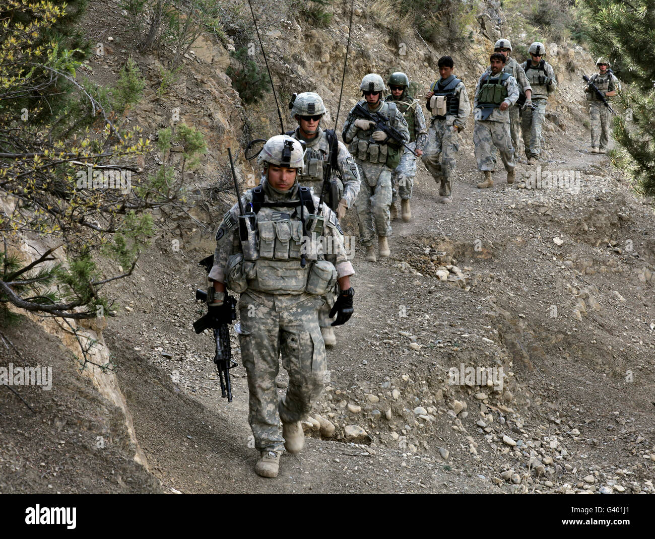 U.S. Soldiers and Afghan Border Policemen walk along a mountain trail in Afghanistan. Stock Photo