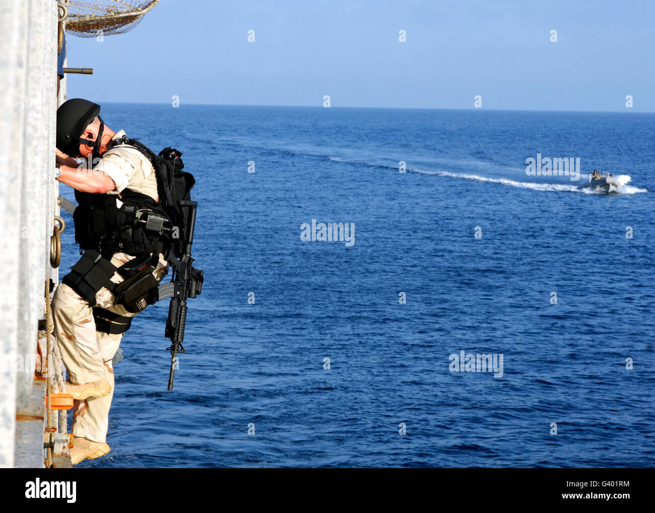 A sailor climbs down the side of the ship into an inflatable boat. Stock Photo
