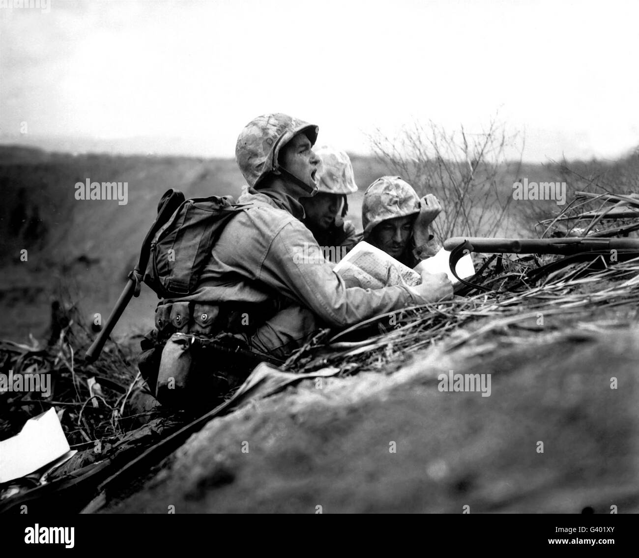 Soldiers locate enemy position on a map while positioned behind a berm. Stock Photo