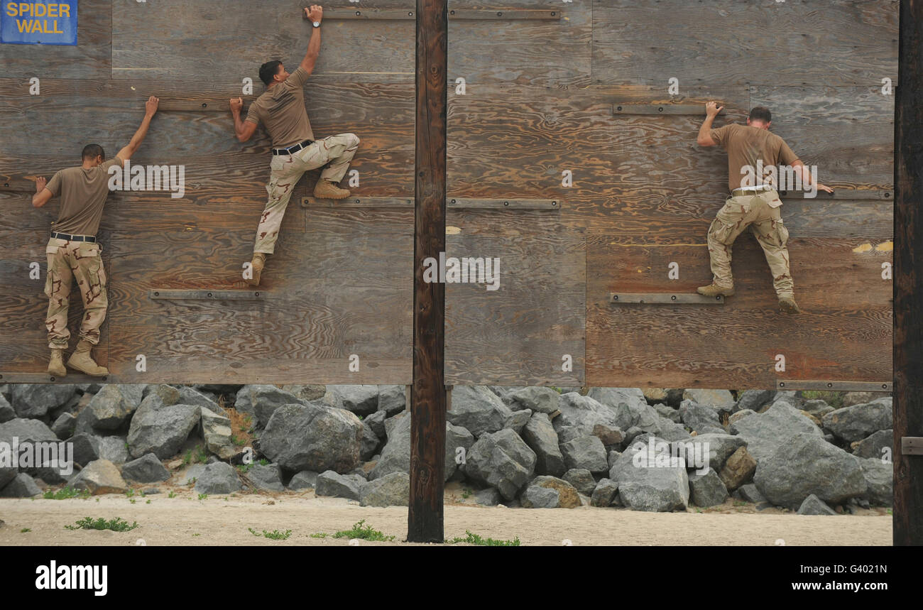 Sailors crawl across narrow planks of wood as part of an obstacle course. Stock Photo