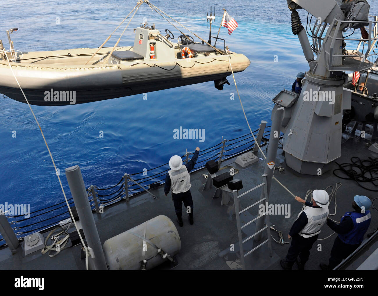 Sailors lower a rigid hull inflatable boat into the water. Stock Photo