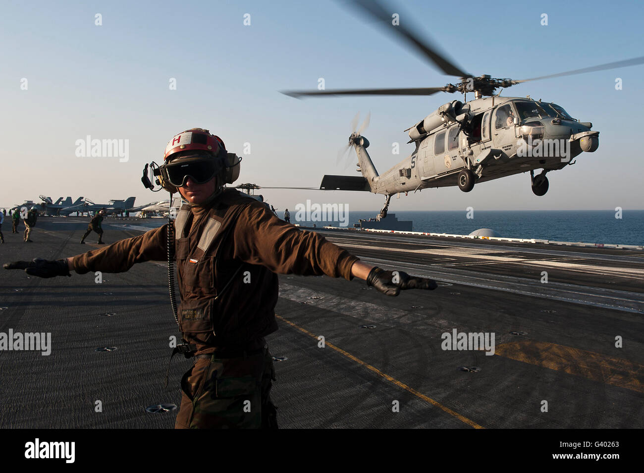 Airman checks for a clear deck as an MH-60S Sea Hawk takes off USS John C. Stennis. Stock Photo