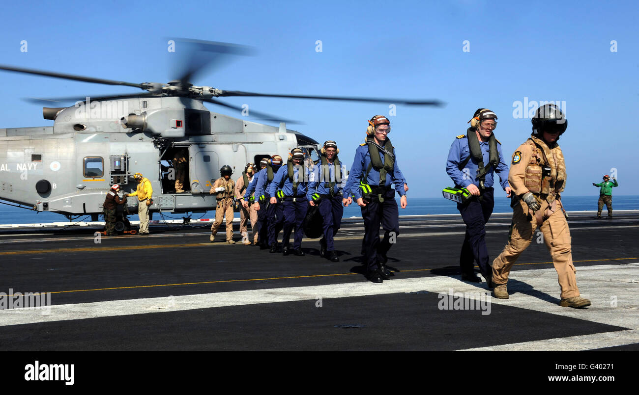 British Sailors are escorted off an EH-101 Merlin helicopter aboard USS John C. Stennis. Stock Photo