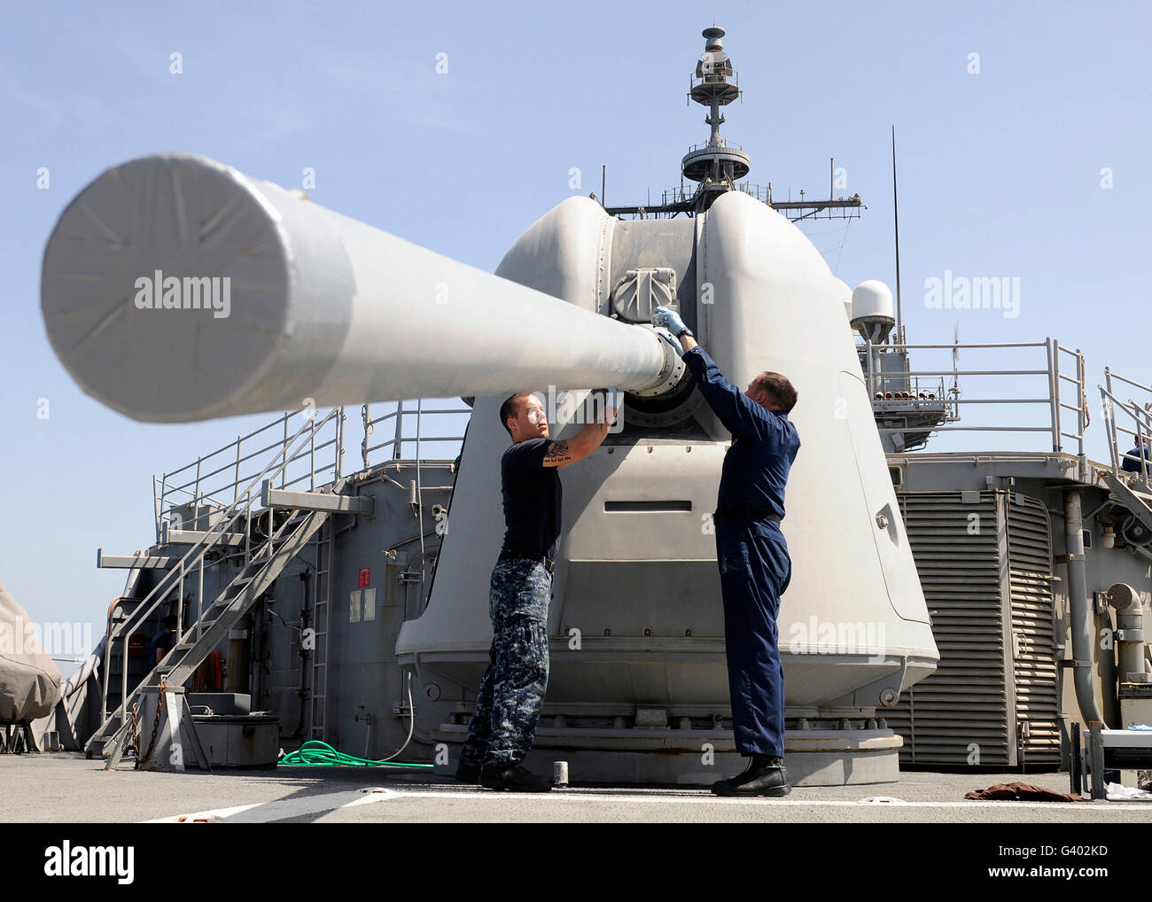 Sailors perform maintenance on a MK-45 5-inch/54-caliber lightweight gun. Stock Photo
