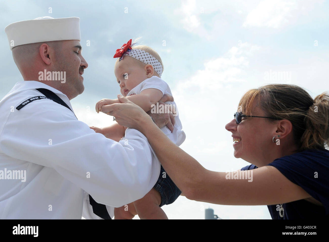 U.S. Navy sailor is handed his eight-month old daughter by his wife at homecoming. Stock Photo