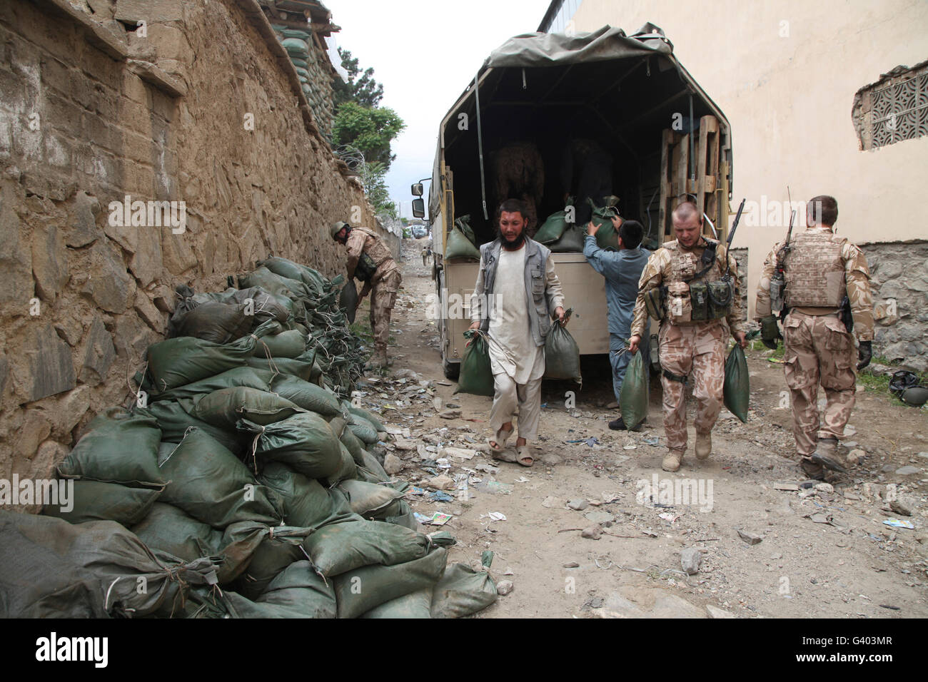 Czech soldiers and Afghan Uniform Police officers unload sandbags from a truck. Stock Photo
