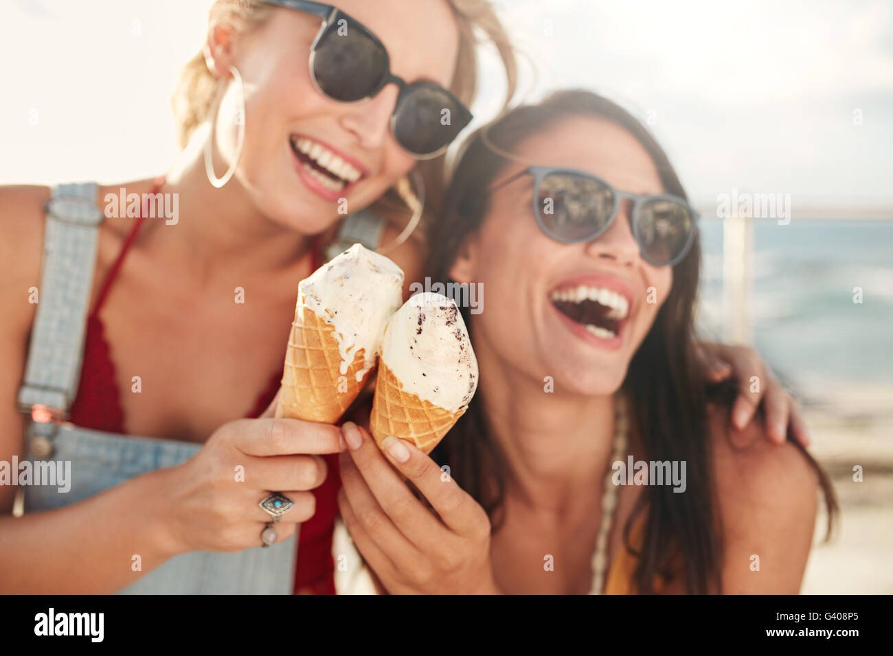 Two young female friends having fun and eating ice cream. Cheerful young women eating icecream outdoors. Stock Photo