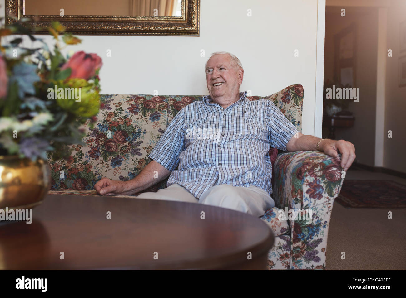 Portrait of a relaxed senior man sitting on a sofa at old age home looking away and smiling Stock Photo