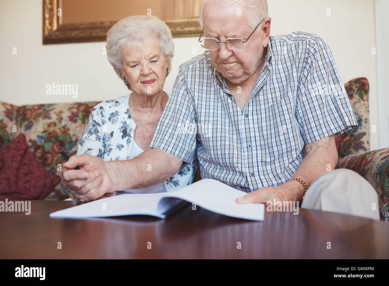 Indoor shot of mature couple at home reading paperwork together. Senior man and woman sitting on sofa going through some retirem Stock Photo